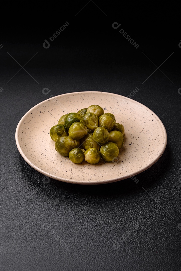 Deliciosas couves de Bruxelas cozidas em um prato de cerâmica sobre um fundo escuro de concreto. Comida vegetariana