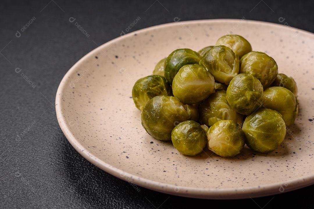 Deliciosas couves de Bruxelas cozidas em um prato de cerâmica sobre um fundo escuro de concreto. Comida vegetariana
