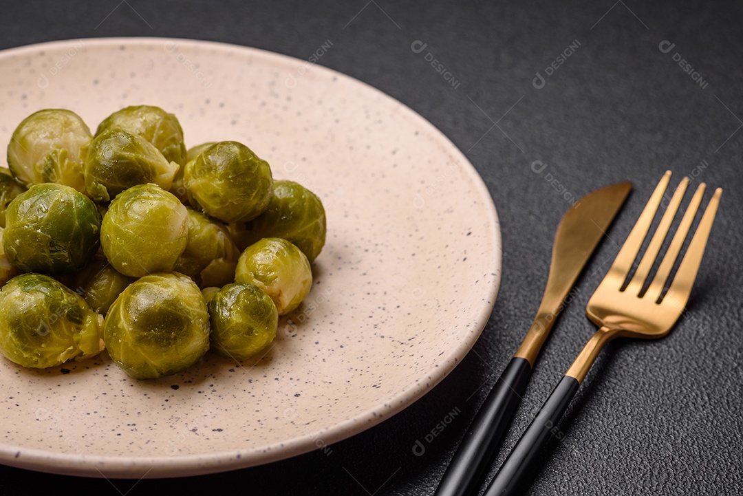 Deliciosas couves de Bruxelas cozidas em um prato de cerâmica sobre um fundo escuro de concreto. Comida vegetariana