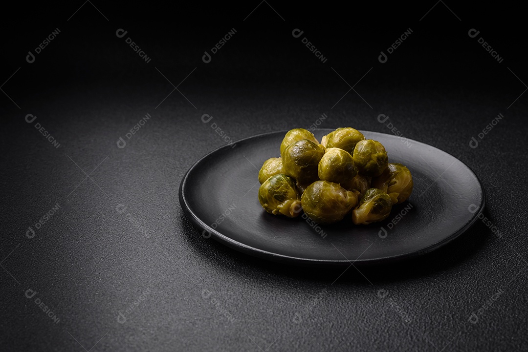 Deliciosas couves de Bruxelas cozidas em um prato de cerâmica sobre um fundo escuro de concreto. Comida vegetariana