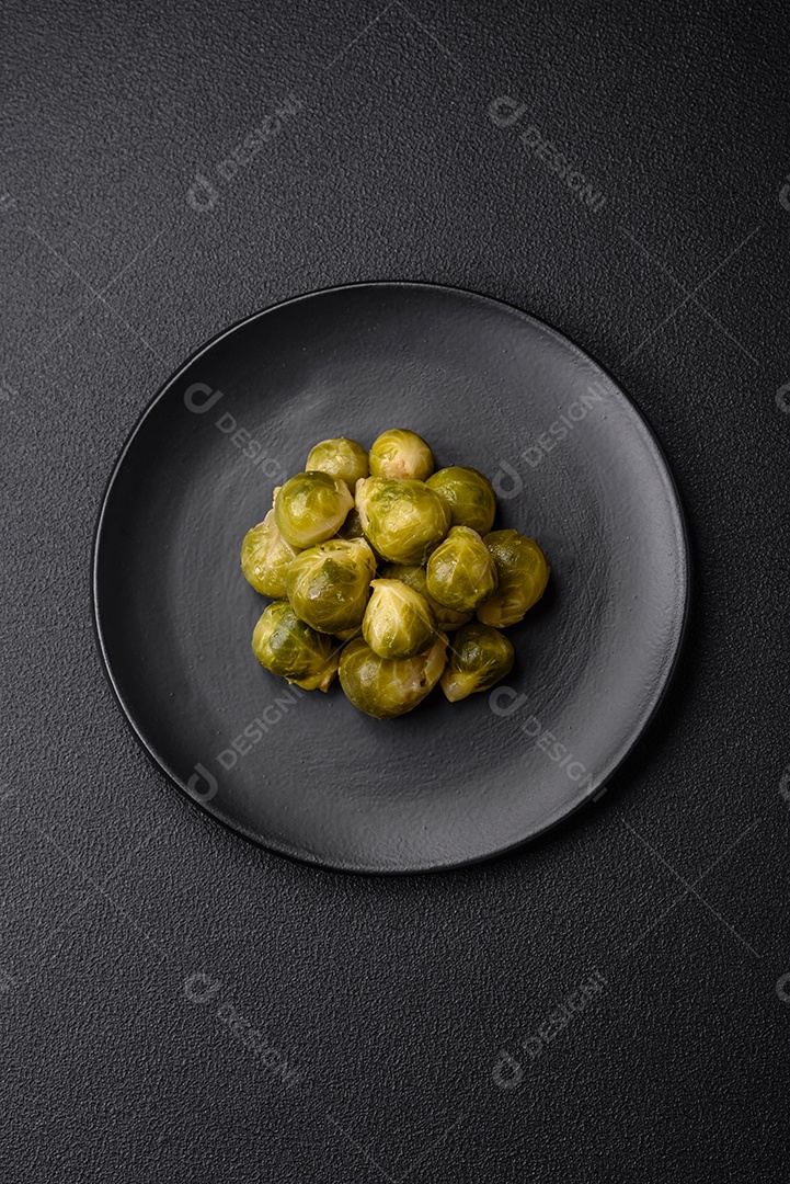 Deliciosas couves de Bruxelas cozidas em um prato de cerâmica sobre um fundo escuro de concreto. Comida vegetariana
