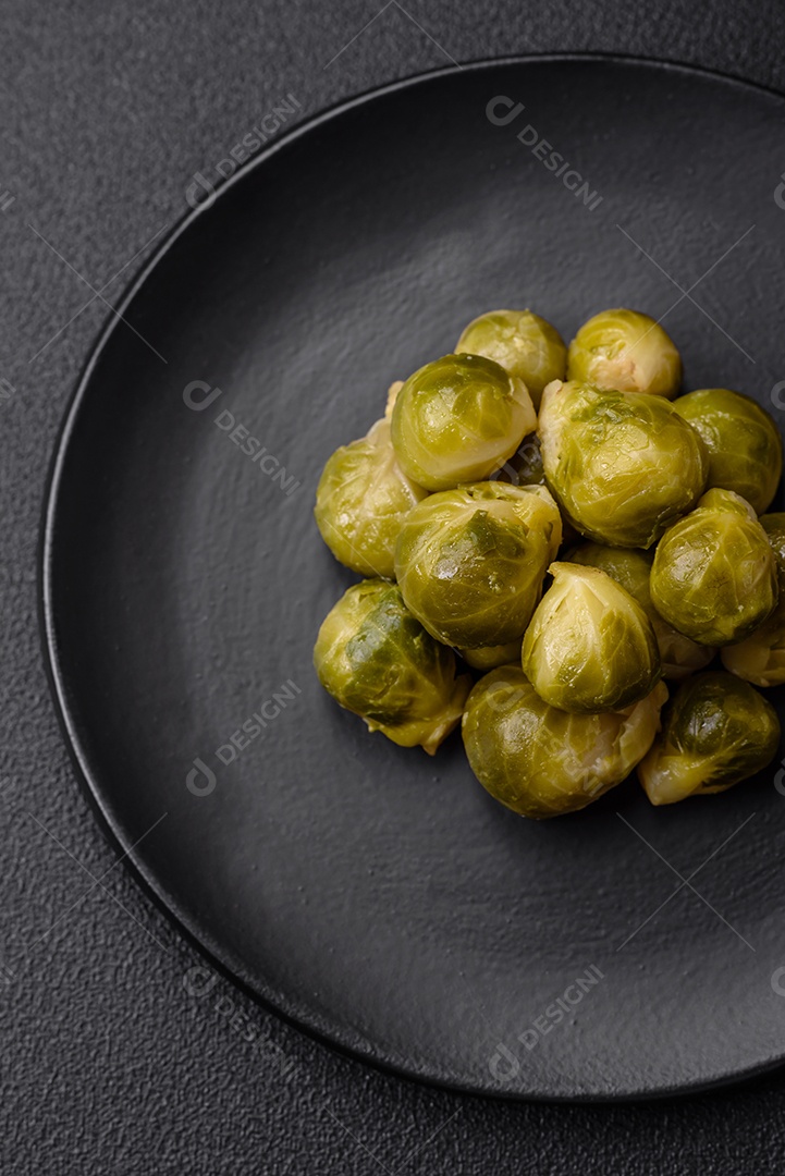 Deliciosas couves de Bruxelas cozidas em um prato de cerâmica sobre um fundo escuro de concreto. Comida vegetariana