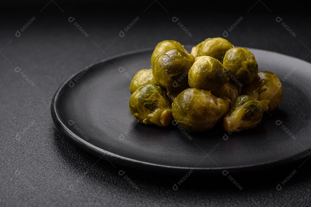 Deliciosas couves de Bruxelas cozidas em um prato de cerâmica sobre um fundo escuro de concreto. Comida vegetariana