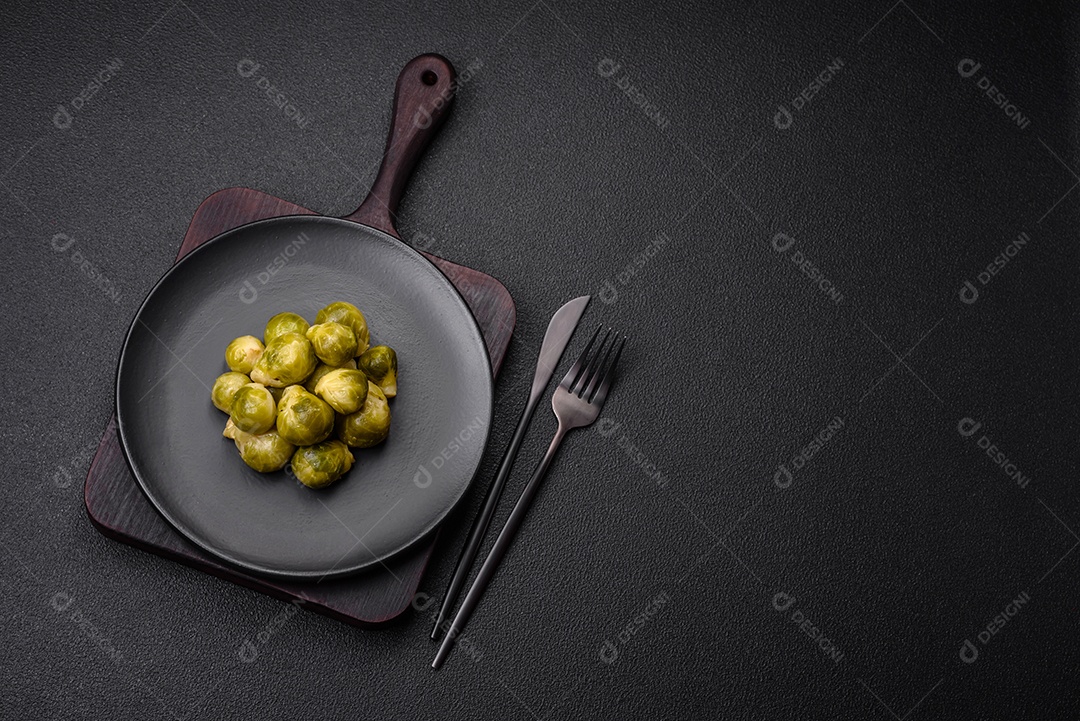 Deliciosas couves de Bruxelas cozidas em um prato de cerâmica sobre um fundo escuro de concreto. Comida vegetariana