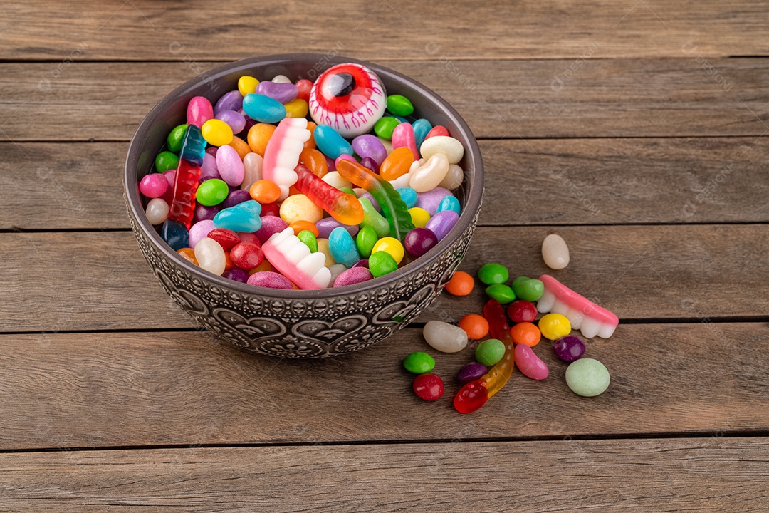 Doces coloridos variados em uma tigela sobre a mesa de madeira.