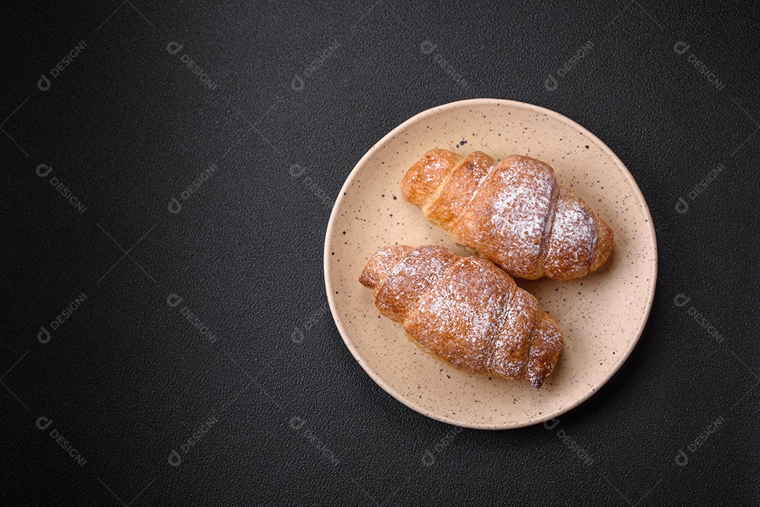 Deliciosos croissants crocantes e frescos com creme de chocolate em uma placa de cerâmica sobre um fundo escuro de concreto