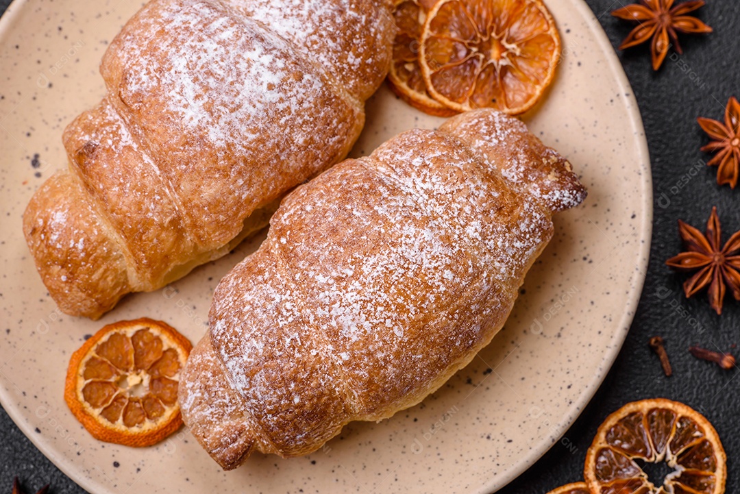 Deliciosos croissants crocantes e frescos com creme de chocolate em uma placa de cerâmica sobre um fundo escuro de concreto