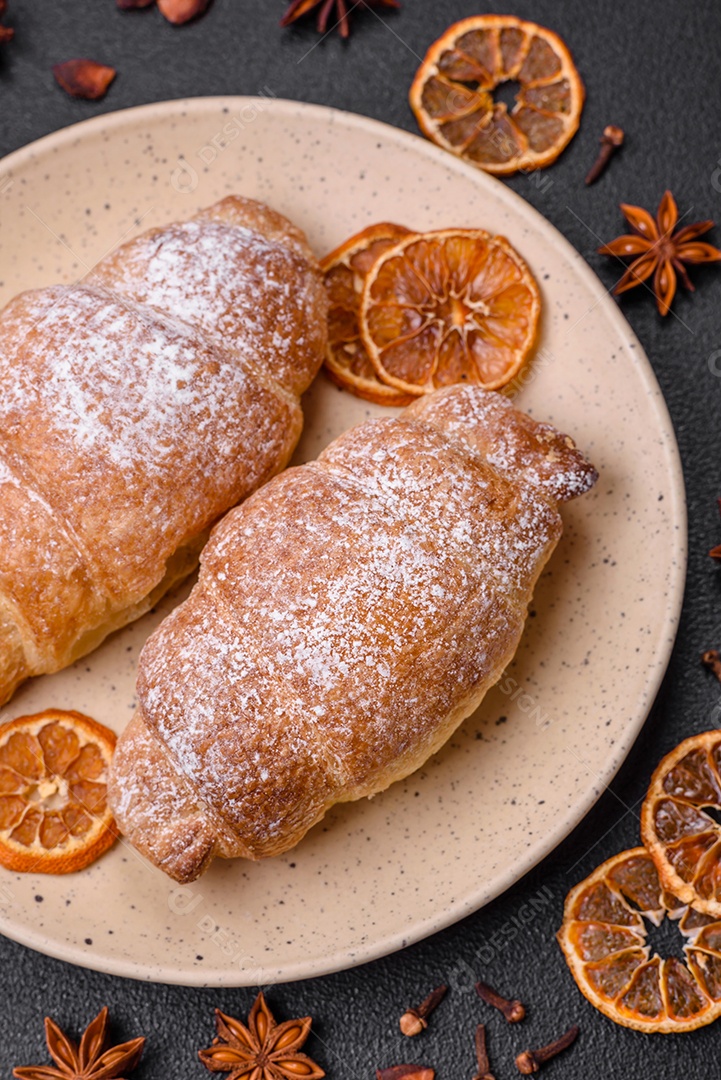 Deliciosos croissants crocantes e frescos com creme de chocolate em uma placa de cerâmica sobre um fundo escuro de concreto