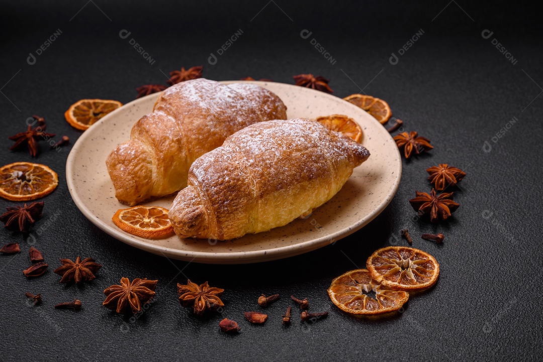 Deliciosos croissants crocantes e frescos com creme de chocolate em uma placa de cerâmica sobre um fundo escuro de concreto