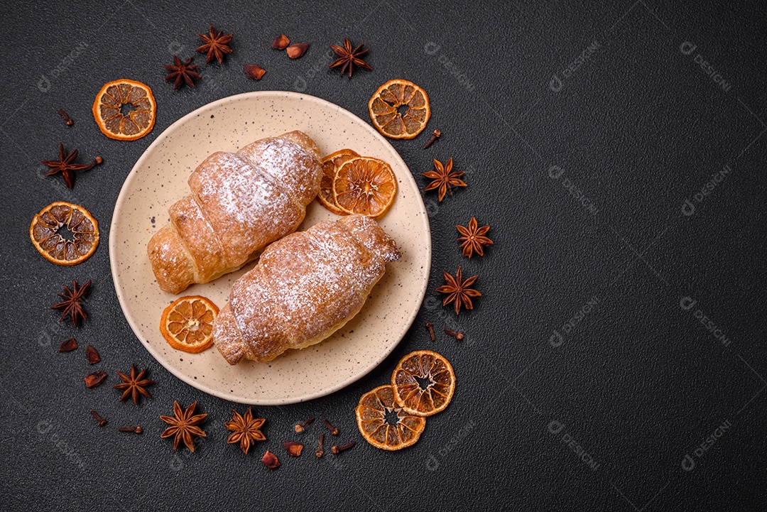 Deliciosos croissants crocantes e frescos com creme de chocolate em uma placa de cerâmica sobre um fundo escuro de concreto