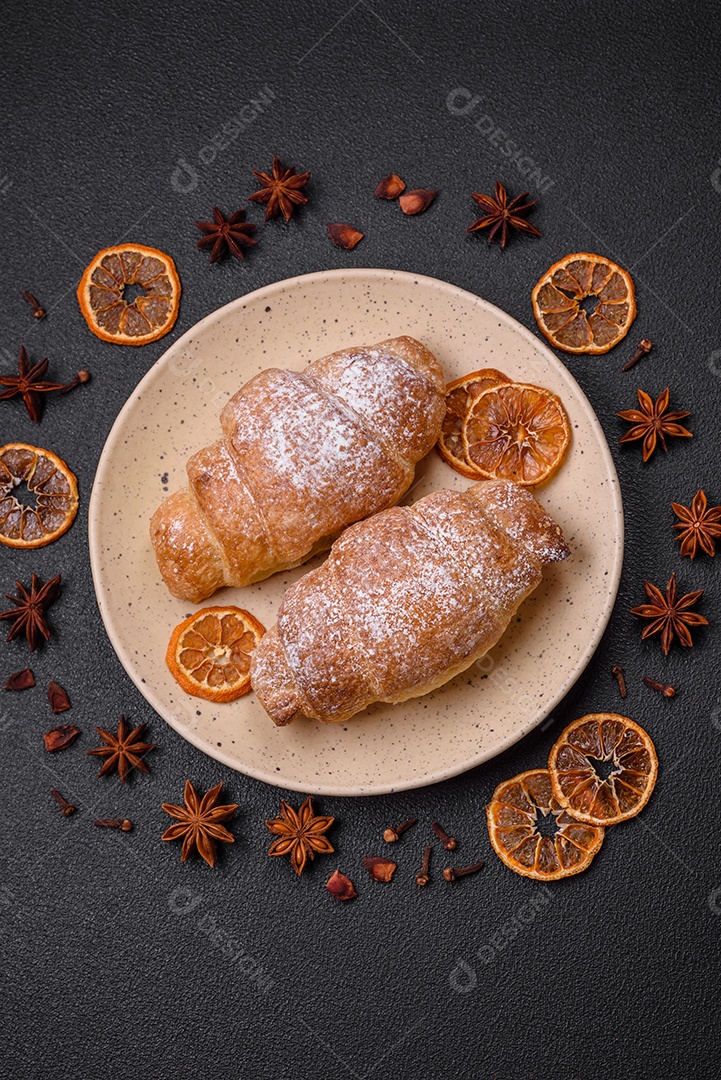 Deliciosos croissants crocantes e frescos com creme de chocolate em uma placa de cerâmica sobre um fundo escuro de concreto