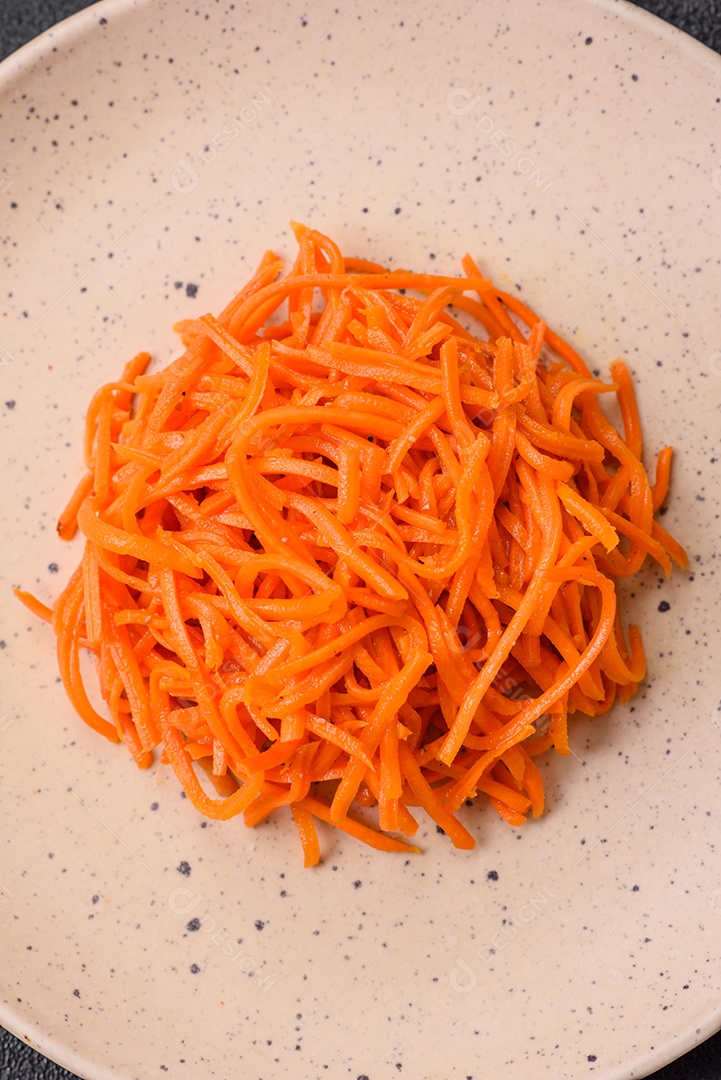 Deliciosas cenouras picantes cortadas e cozidas em estilo coreano em uma placa cerâmica sobre um fundo escuro de concreto