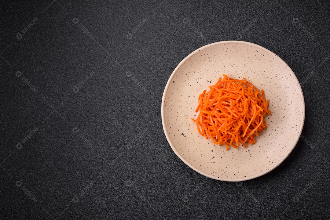 Deliciosas cenouras picantes cortadas e cozidas em estilo coreano em uma placa cerâmica sobre um fundo escuro de concreto