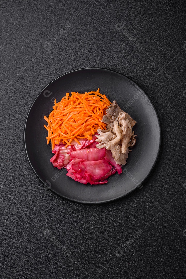 Deliciosos cogumelos picantes, cenouras, repolho fatiado e cozido em estilo coreano em uma placa cerâmica sobre um fundo escuro de concreto