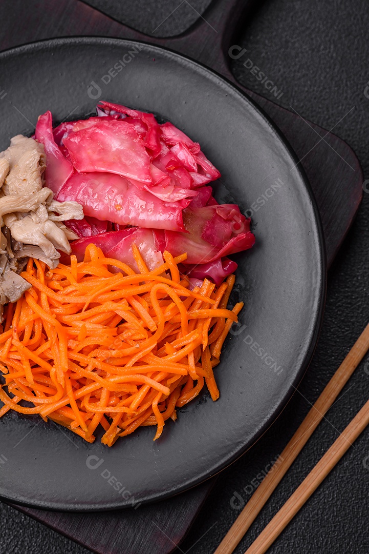 Deliciosos cogumelos picantes, cenouras, repolho fatiado e cozido em estilo coreano em uma placa cerâmica sobre um fundo escuro de concreto