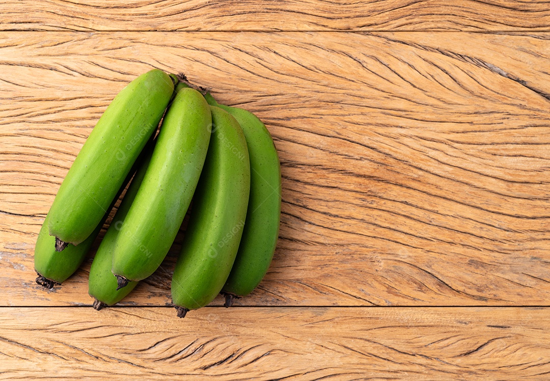 Um cacho de bananas verdes sobre uma mesa de madeira com espaço de cópia.