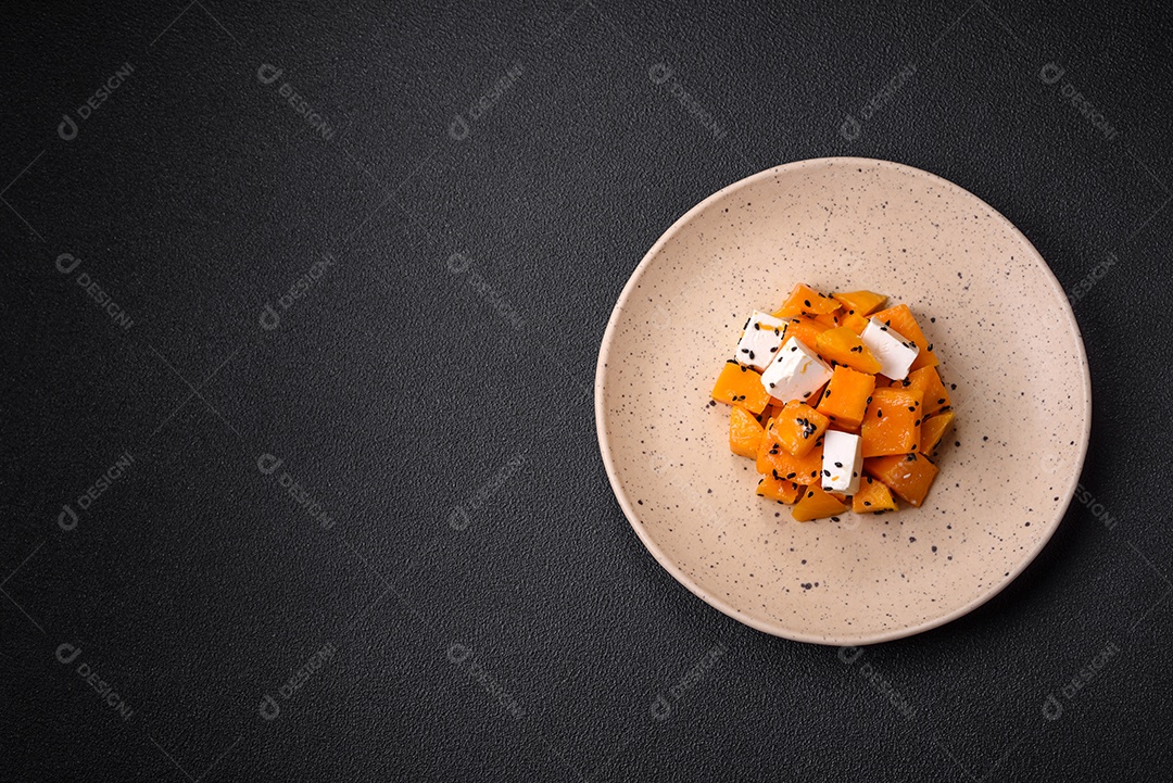 Deliciosa salada suculenta de abóbora grelhada em cubos com queijo feta, especiarias e sementes de gergelim num prato cerâmico