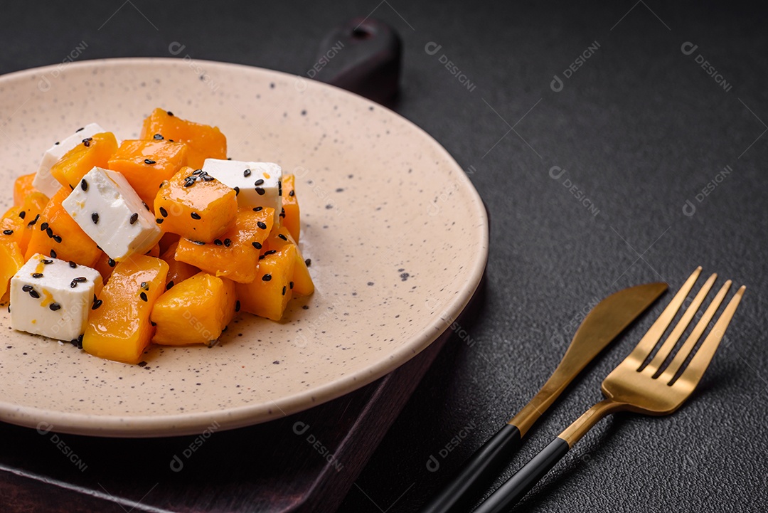 Deliciosa salada suculenta de abóbora grelhada em cubos com queijo feta, especiarias e sementes de gergelim num prato cerâmico