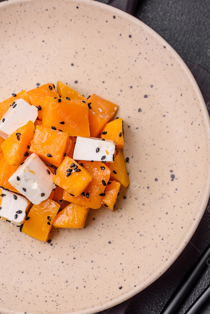 Deliciosa salada suculenta de abóbora grelhada em cubos com queijo feta, especiarias e sementes de gergelim num prato cerâmico