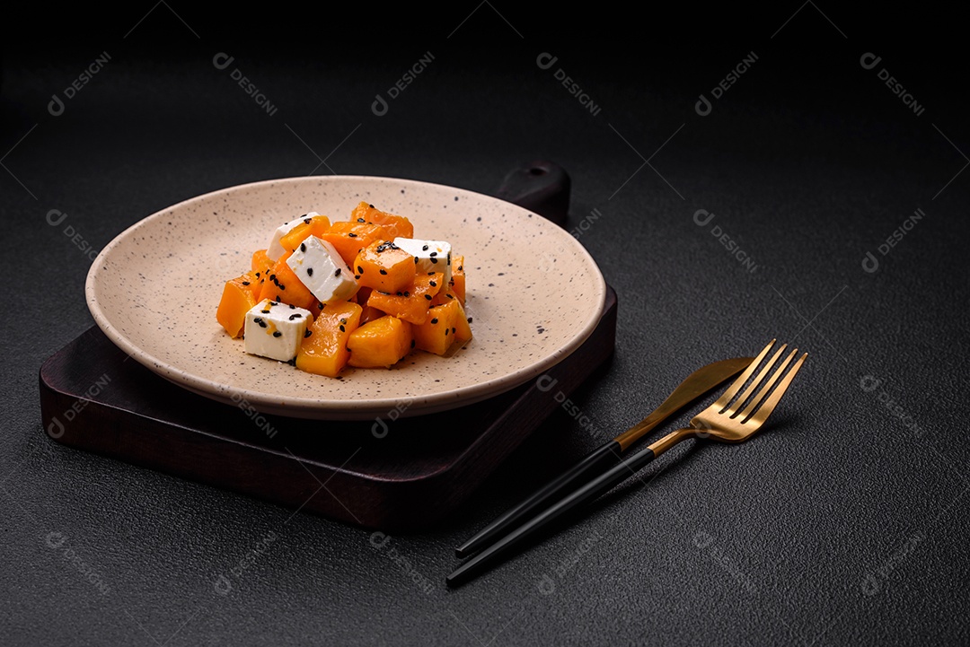 Deliciosa salada suculenta de abóbora grelhada em cubos com queijo feta, especiarias e sementes de gergelim num prato cerâmico
