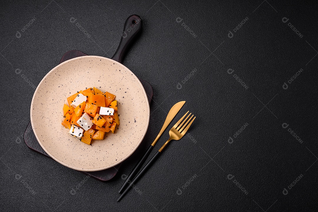 Deliciosa salada suculenta de abóbora grelhada em cubos com queijo feta, especiarias e sementes de gergelim num prato cerâmico