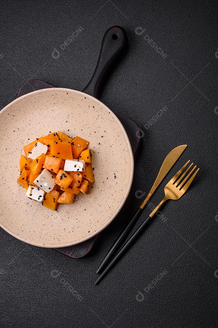 Deliciosa salada suculenta de abóbora grelhada em cubos com queijo feta, especiarias e sementes de gergelim num prato cerâmico