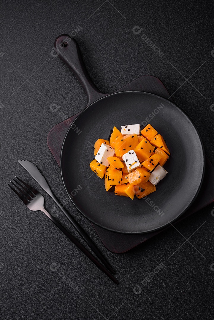 Deliciosa salada suculenta de abóbora grelhada em cubos com queijo feta, especiarias e sementes de gergelim num prato cerâmico