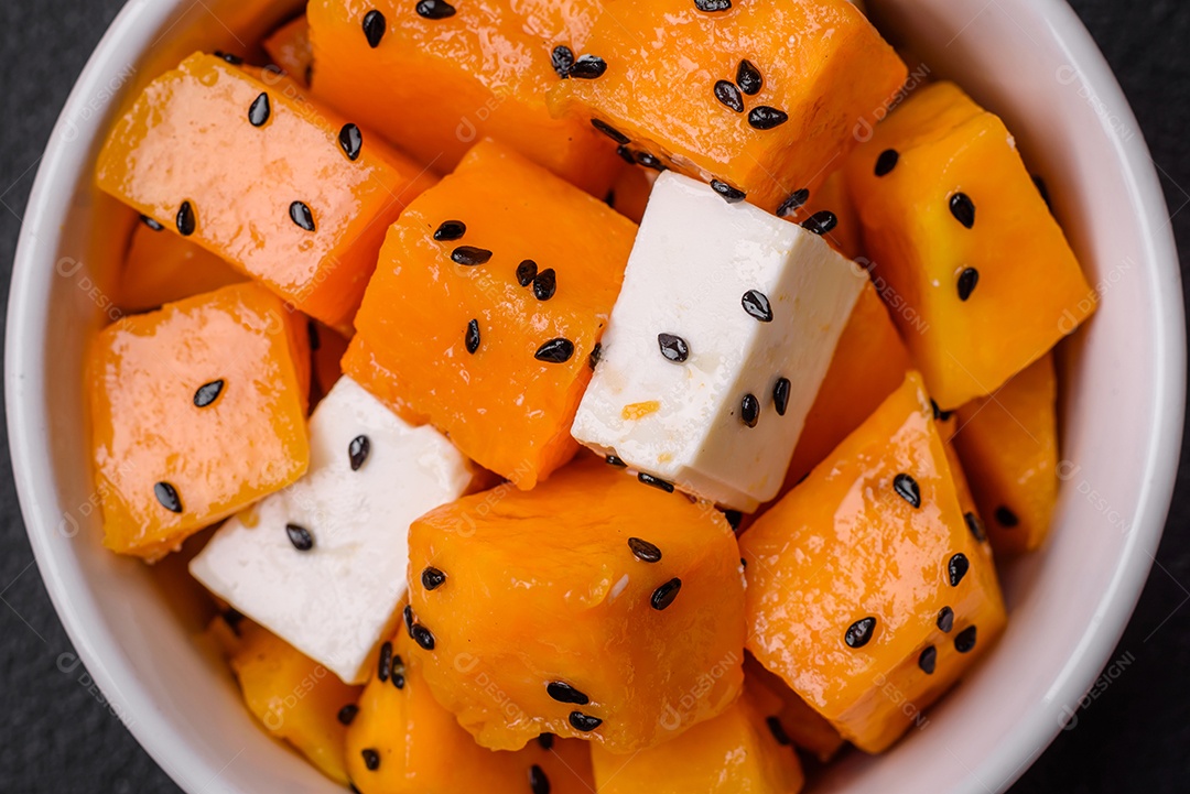 Deliciosa salada suculenta de abóbora grelhada em cubos com queijo feta, especiarias e sementes de gergelim num prato cerâmico