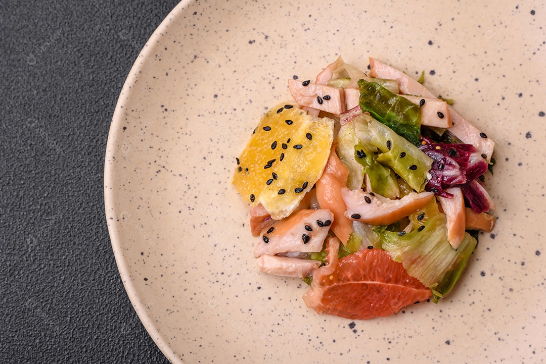 Deliciosa salada fresca e suculenta de frango fatiado, toranja, alface, gergelim com azeite em uma placa cerâmica sobre um fundo de concreto