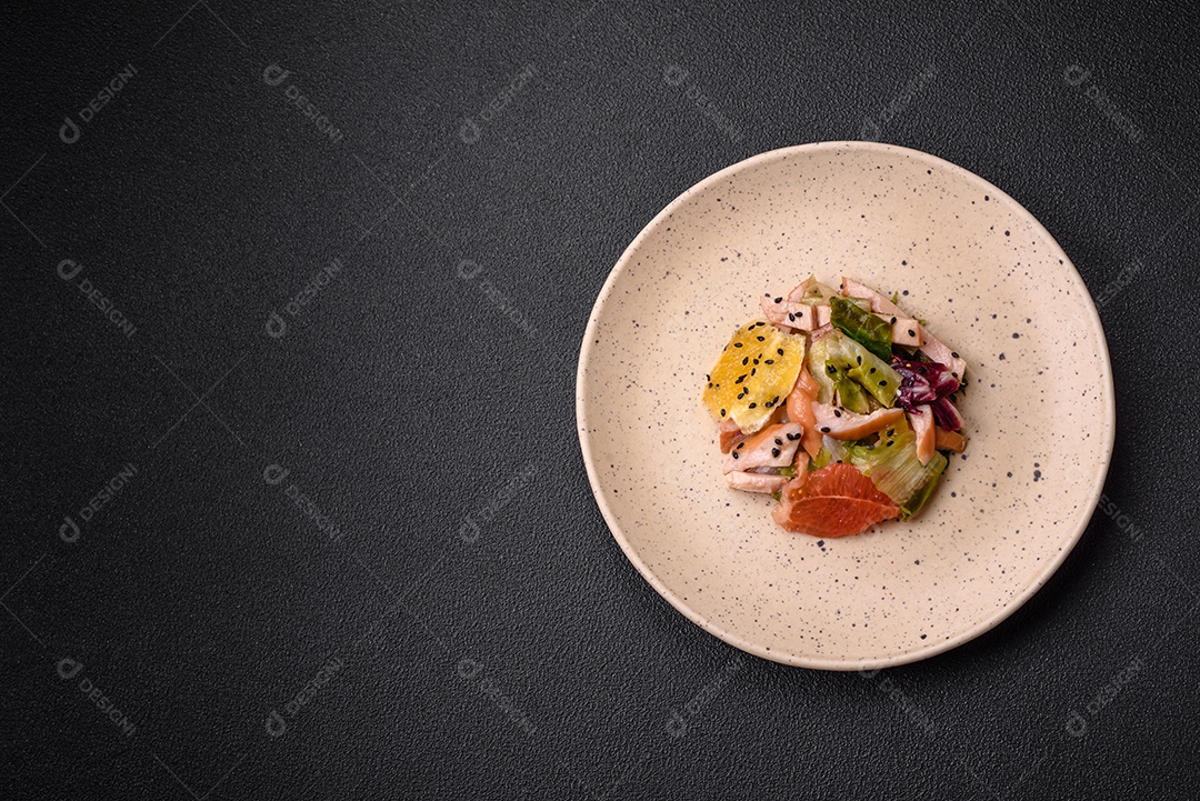 Deliciosa salada fresca e suculenta de frango fatiado, toranja, alface, gergelim com azeite em uma placa cerâmica sobre um fundo de concreto