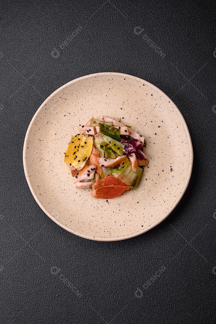 Deliciosa salada fresca e suculenta de frango fatiado, toranja, alface, gergelim com azeite em uma placa cerâmica sobre um fundo de concreto
