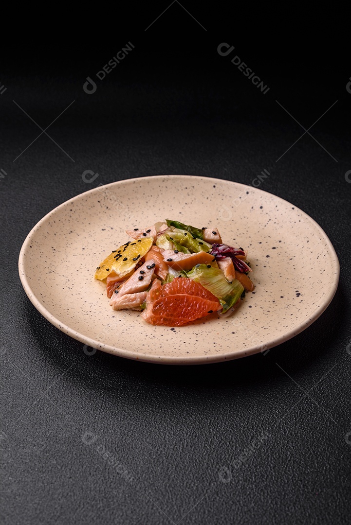Deliciosa salada fresca e suculenta de frango fatiado, toranja, alface, gergelim com azeite em uma placa cerâmica sobre um fundo de concreto