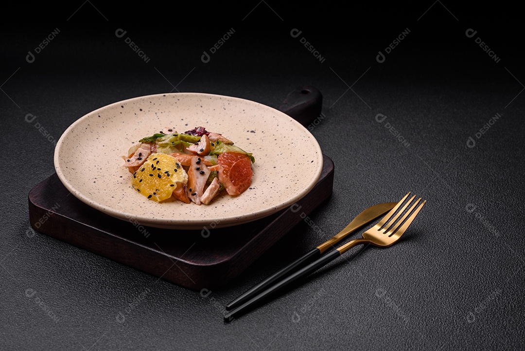 Deliciosa salada fresca e suculenta de frango fatiado, toranja, alface, gergelim com azeite em uma placa cerâmica sobre um fundo de concreto