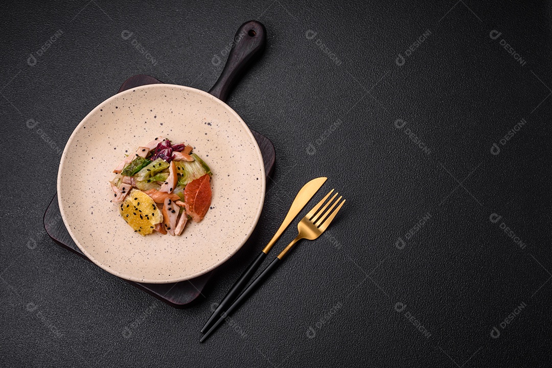 Deliciosa salada fresca e suculenta de frango fatiado, toranja, alface, gergelim com azeite em uma placa cerâmica sobre um fundo de concreto