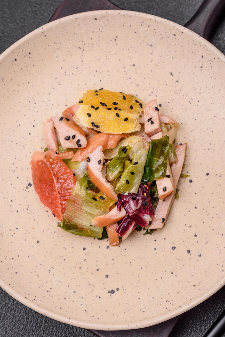 Deliciosa salada fresca e suculenta de frango fatiado, toranja, alface, gergelim com azeite em uma placa cerâmica sobre um fundo de concreto