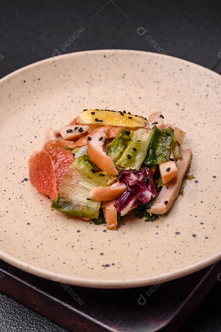 Deliciosa salada fresca e suculenta de frango fatiado, toranja, alface, gergelim com azeite em uma placa cerâmica sobre um fundo de concreto