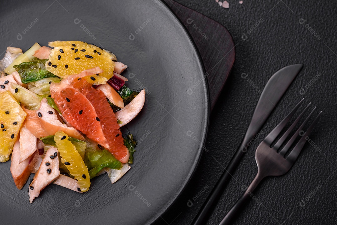 Deliciosa salada fresca e suculenta de frango fatiado, toranja, alface, gergelim com azeite em uma placa cerâmica sobre um fundo de concreto