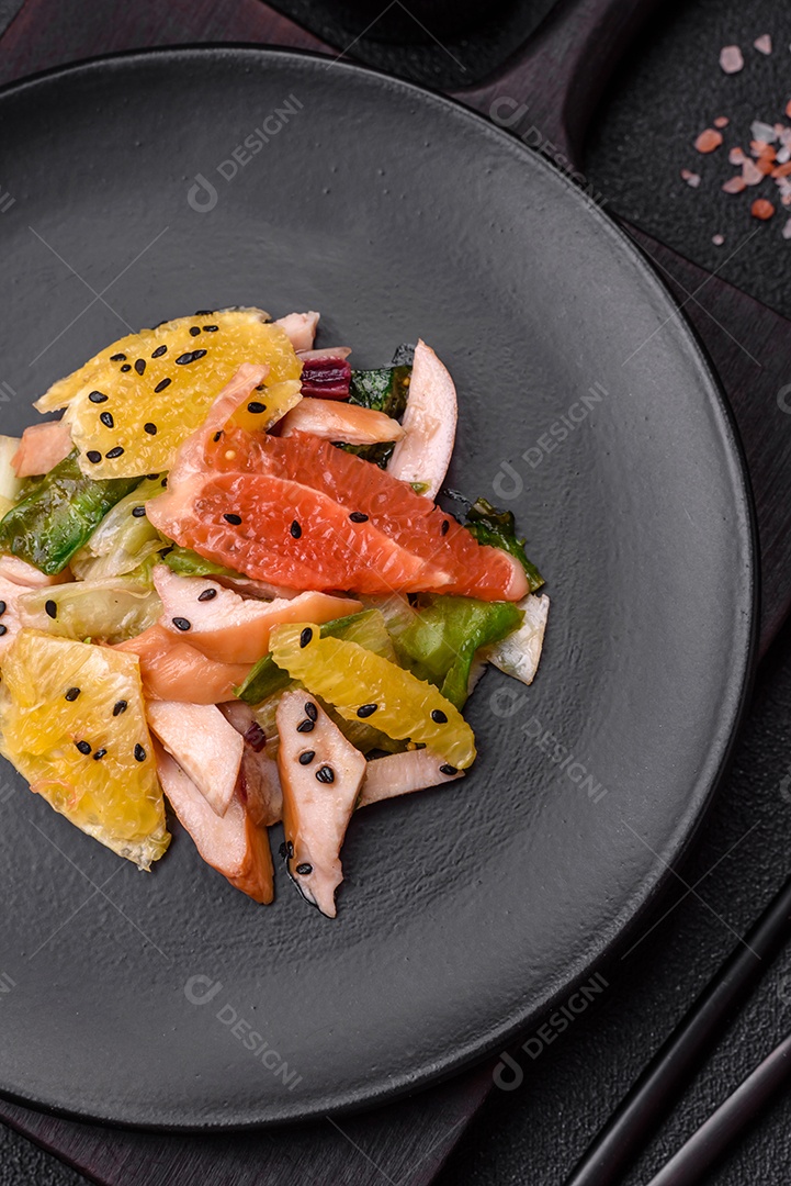 Deliciosa salada fresca e suculenta de frango fatiado, toranja, alface, gergelim com azeite em uma placa cerâmica sobre um fundo de concreto
