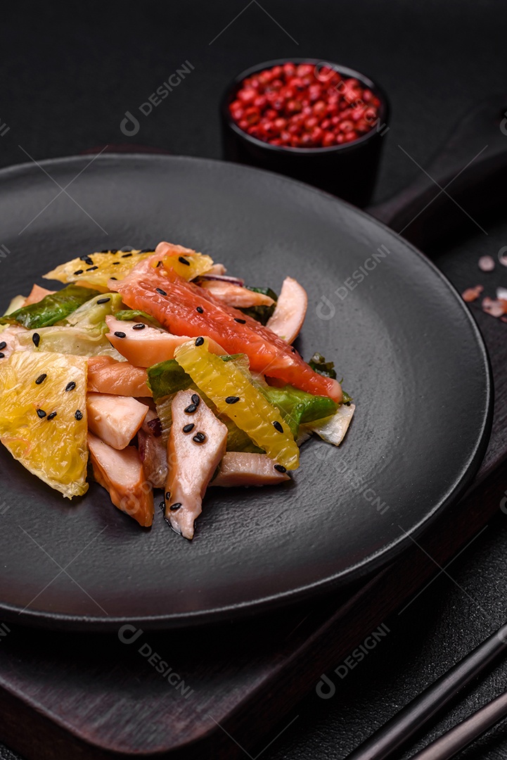 Deliciosa salada fresca e suculenta de frango fatiado, toranja, alface, gergelim com azeite em uma placa cerâmica sobre um fundo de concreto
