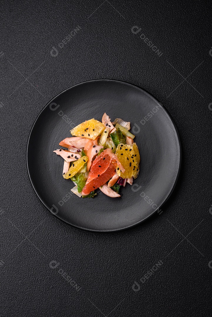 Deliciosa salada fresca e suculenta de frango fatiado, toranja, alface, gergelim com azeite em uma placa cerâmica sobre um fundo de concreto