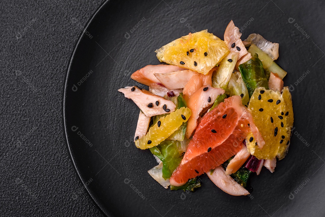 Deliciosa salada fresca e suculenta de frango fatiado, toranja, alface, gergelim com azeite em uma placa cerâmica sobre um fundo de concreto