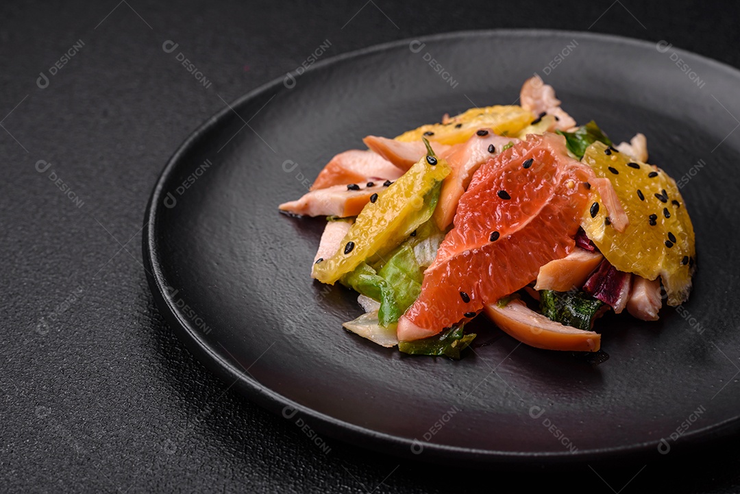 Deliciosa salada fresca e suculenta de frango fatiado, toranja, alface, gergelim com azeite em uma placa cerâmica sobre um fundo de concreto
