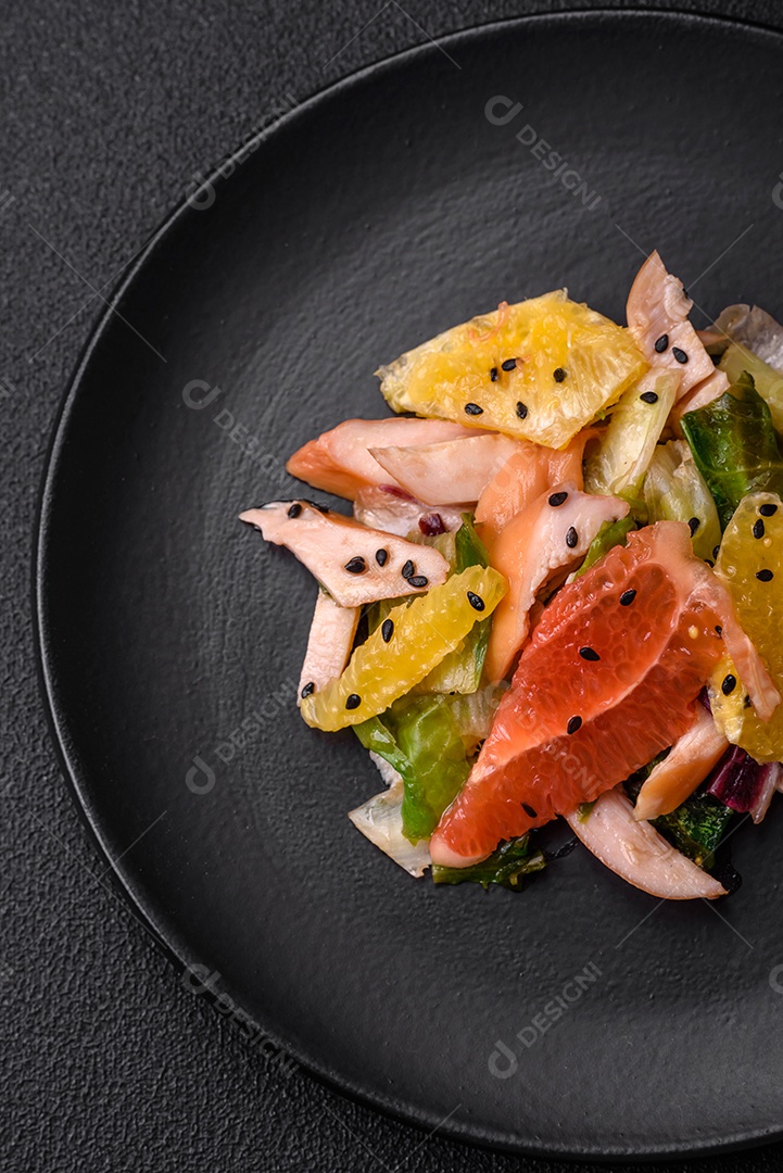 Deliciosa salada fresca e suculenta de frango fatiado, toranja, alface, gergelim com azeite em uma placa cerâmica sobre um fundo de concreto