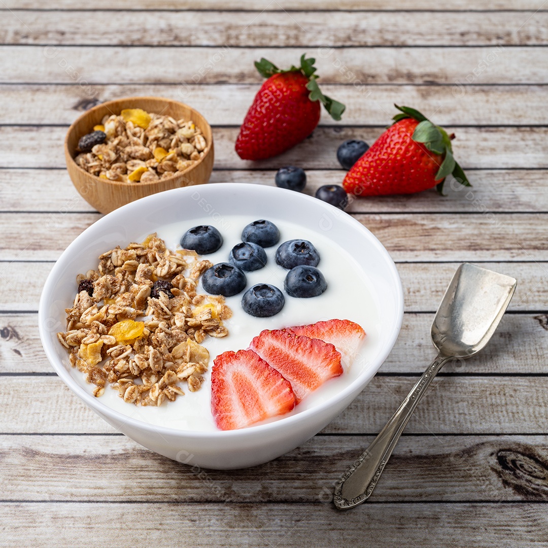 Iogurte com morango, mirtilo e granola em uma tigela sobre a mesa de madeira.