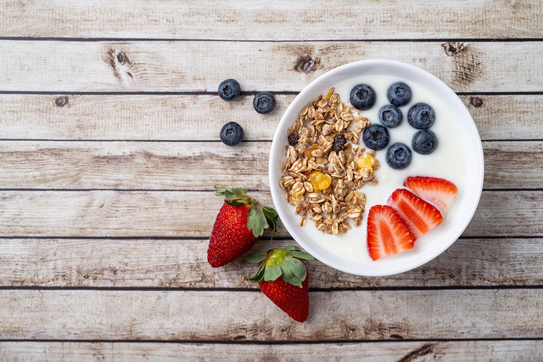 Iogurte com morango, mirtilo e granola em uma tigela sobre a mesa de madeira.