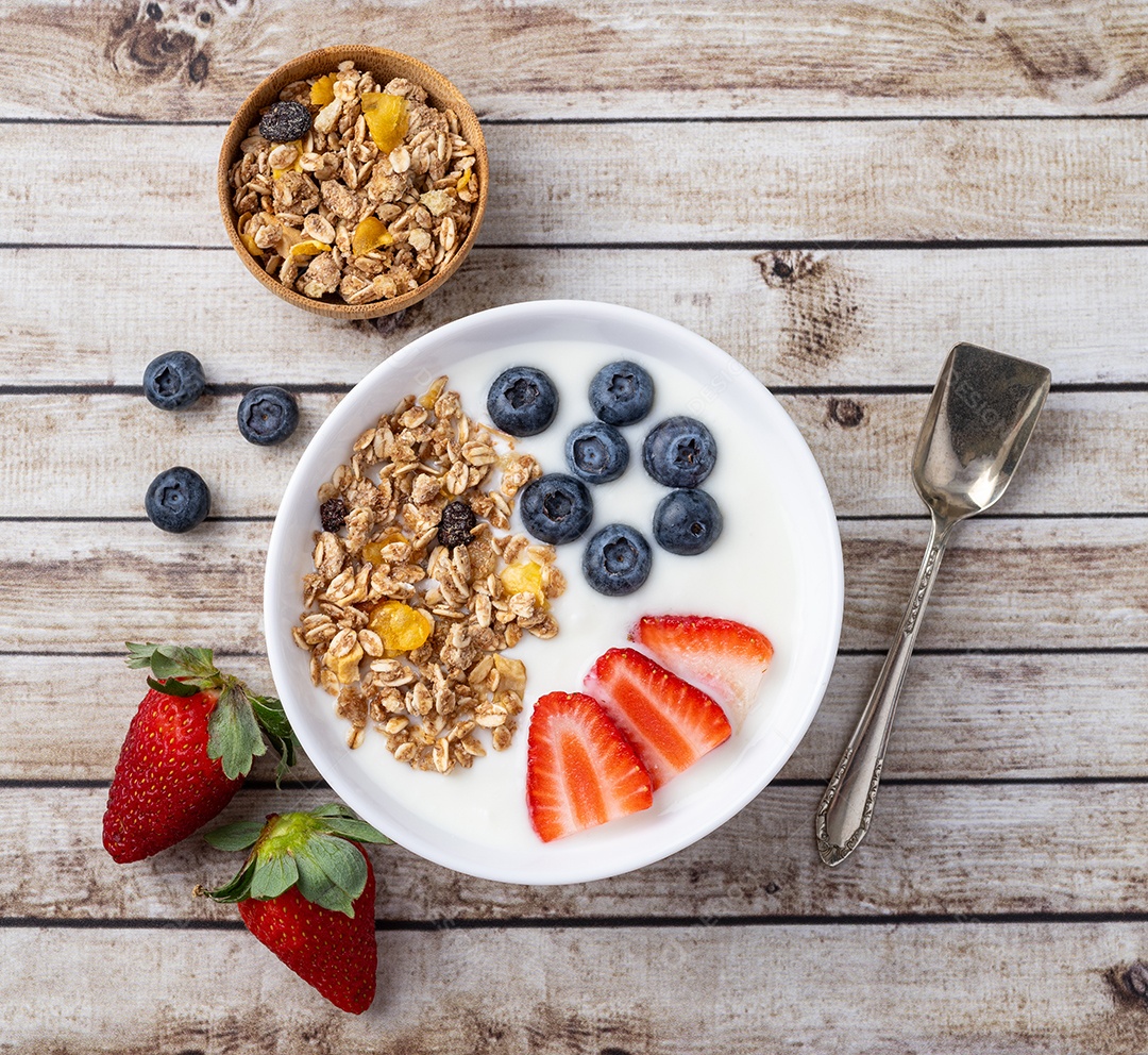 Iogurte com morango, mirtilo e granola em uma tigela sobre a mesa de madeira.
