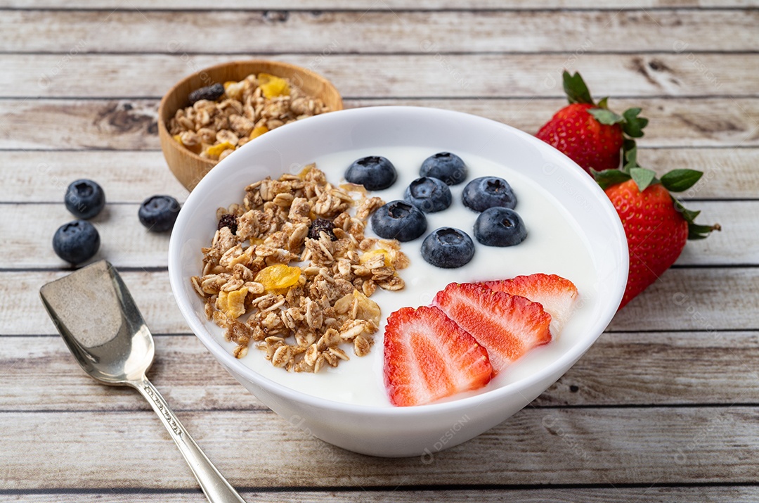Iogurte com morango, mirtilo e granola em uma tigela sobre a mesa de madeira.