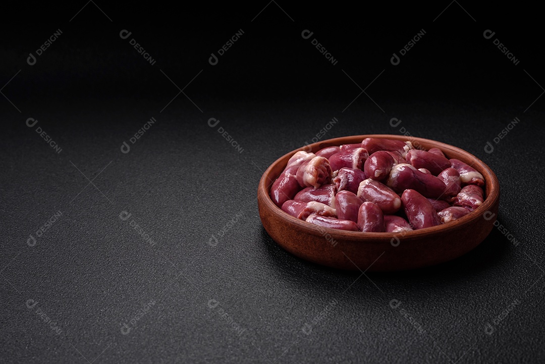 Corações frescos de frango cru, peru ou pato em uma placa de cerâmica com sal e especiarias sobre um fundo escuro de concreto