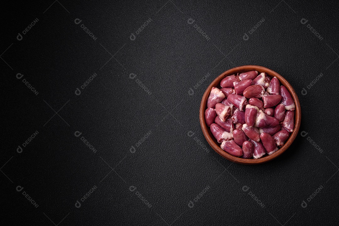 Corações frescos de frango cru, peru ou pato em uma placa de cerâmica com sal e especiarias sobre um fundo escuro de concreto