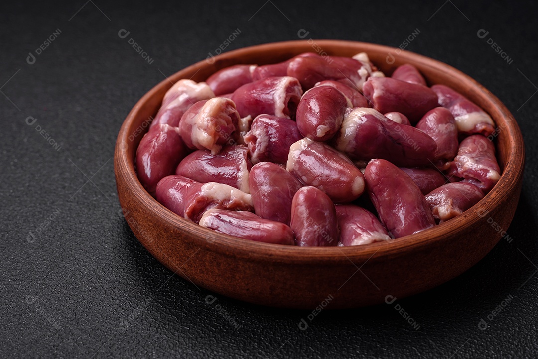 Corações frescos de frango cru, peru ou pato em uma placa de cerâmica com sal e especiarias sobre um fundo escuro de concreto